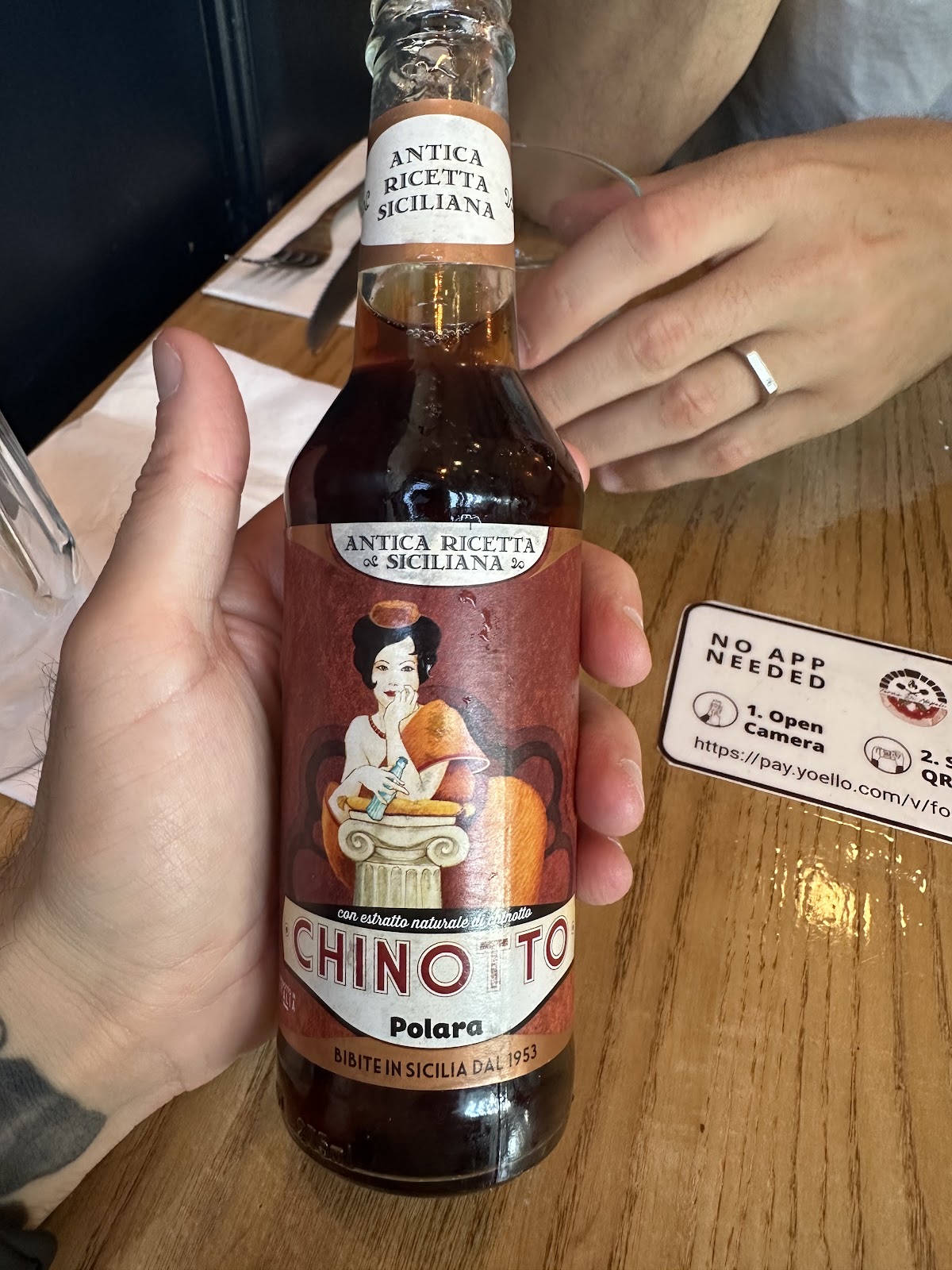 A hand holding a bottle of Sicilian chinotto over the table