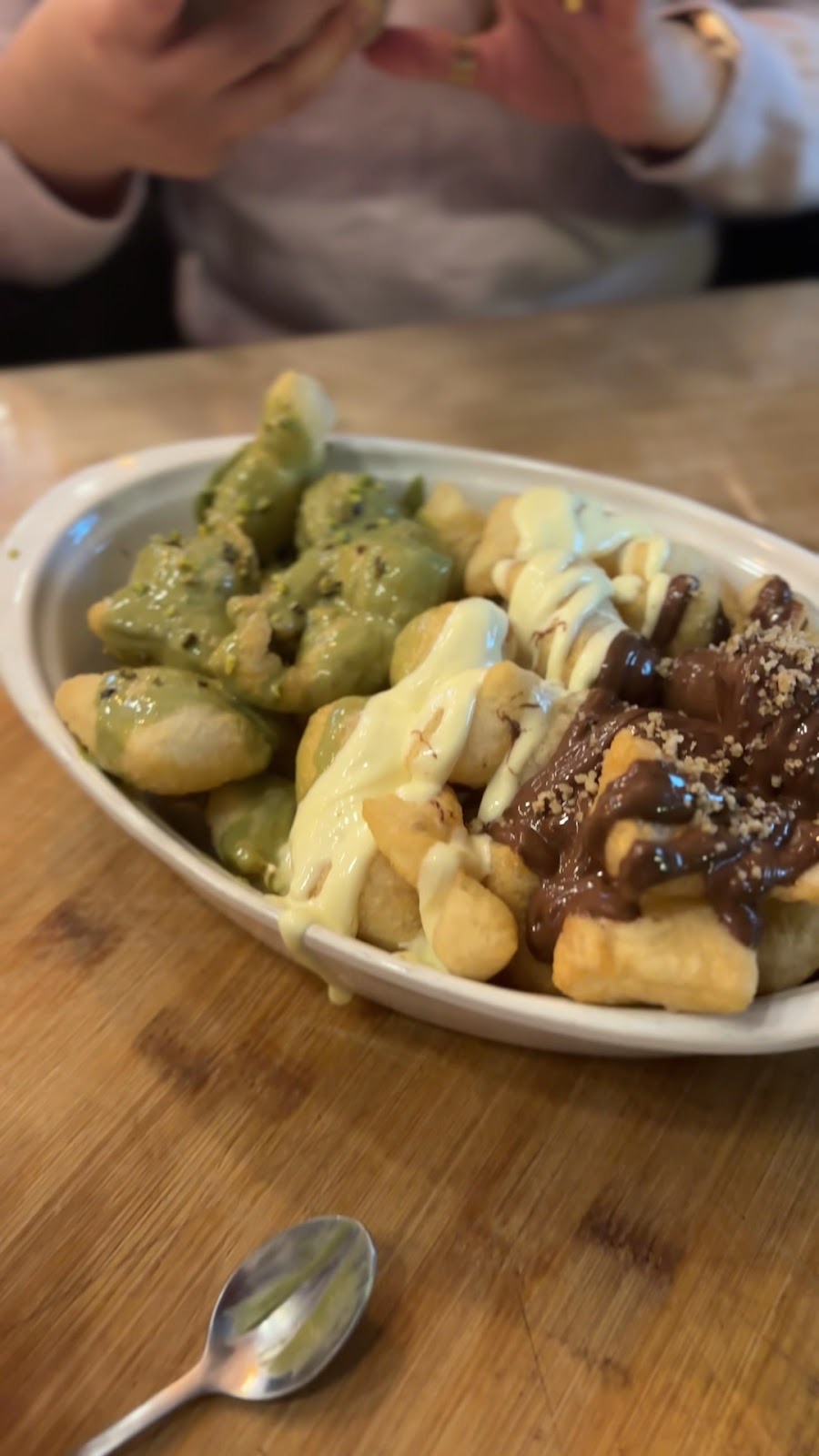 Shared bowl of gnocchi in three sauces on a wooden table