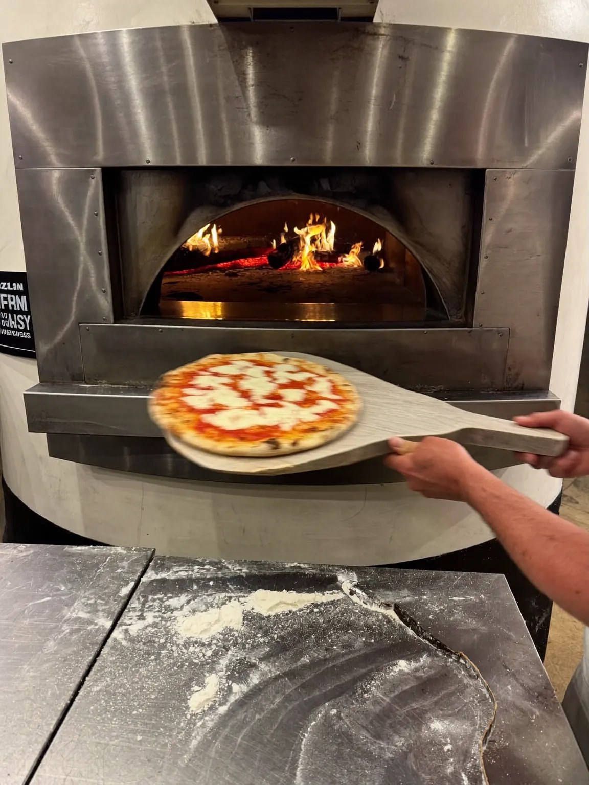 Hands sliding a pizza into a wood-fired oven
