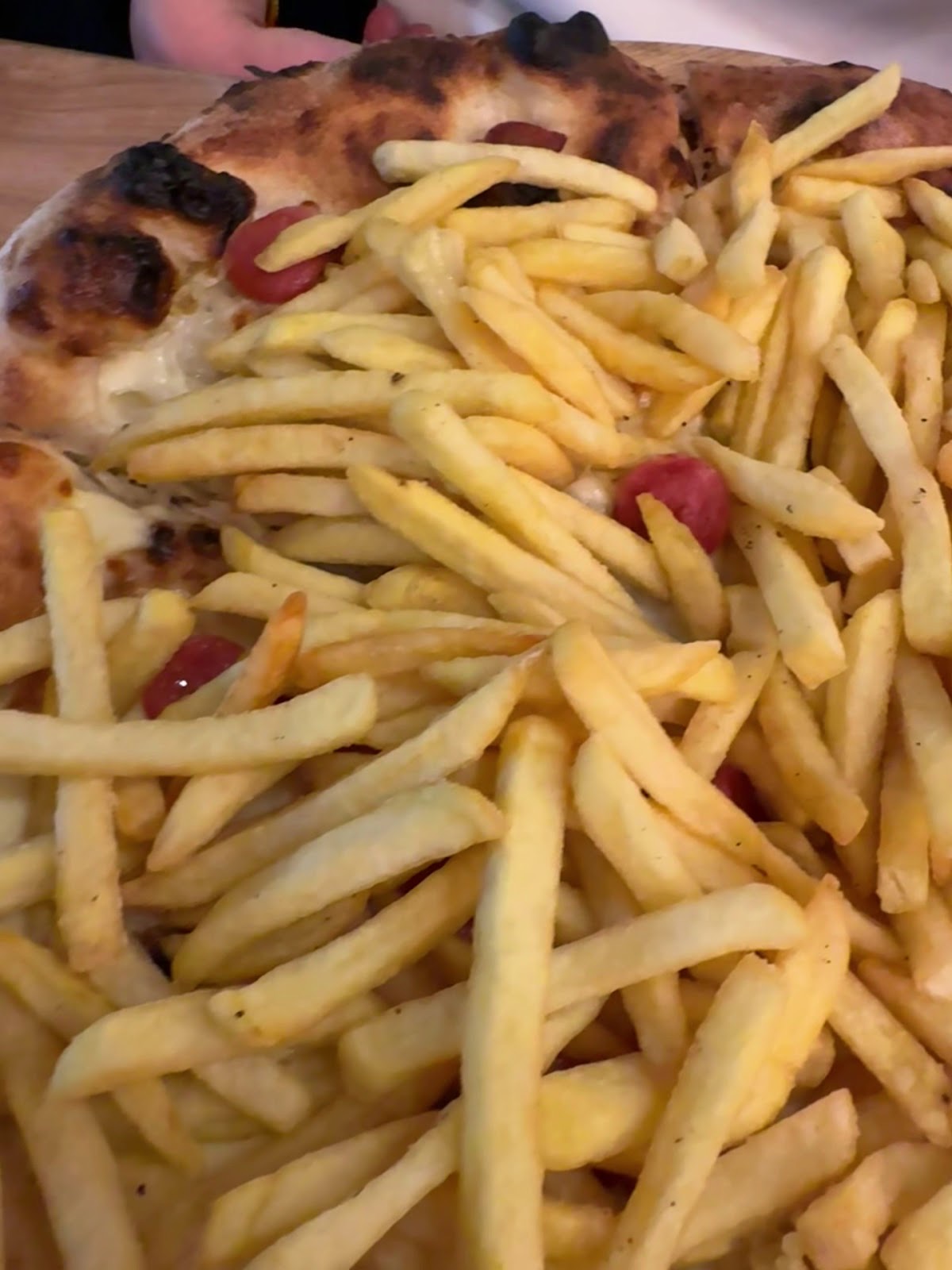 Close shot of a pile of skinny fries beside the edge of a pizza